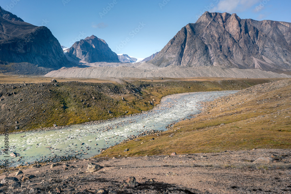 Wild Owl River winds through remote arctic landscape in Akshayuk Pass, Baffin Island, Canada. Moss valley floor and dramatic cliffs. Sunny day of arctic summer in remote wilderness far north.