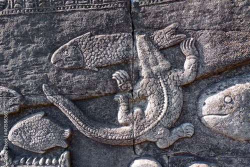 A crocodile hunting a fish is realistically sculpted in stone exterior wall of Bayon Temple, a historic UNESCO ancient heritage site located near Angkor Wat in Cambodia
