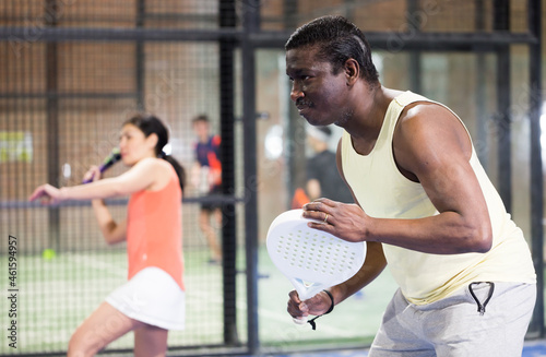 Concentrated american man padel player hitting ball with a racket at fitness health club