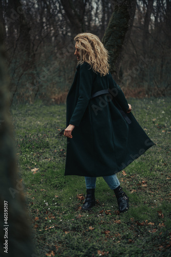 Young blonde woman walking in the woods in a green coat