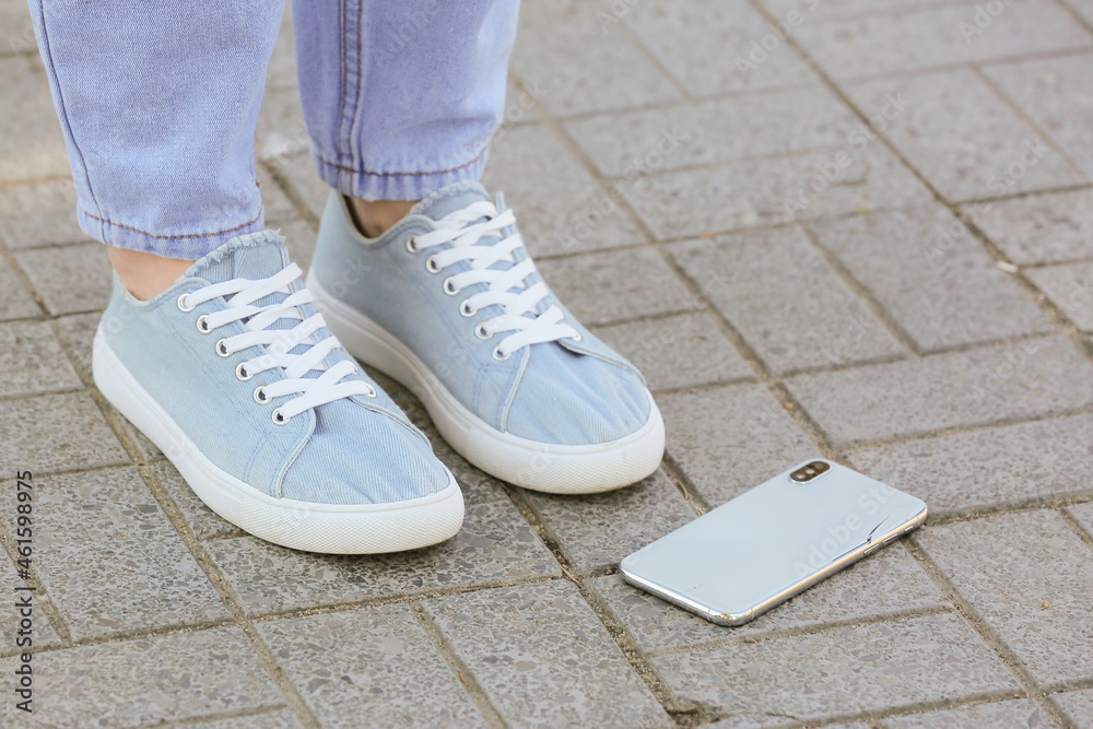 Legs of woman and damaged mobile phone outdoors, closeup Legs of woman and damaged mobile phone outdoors, closeup