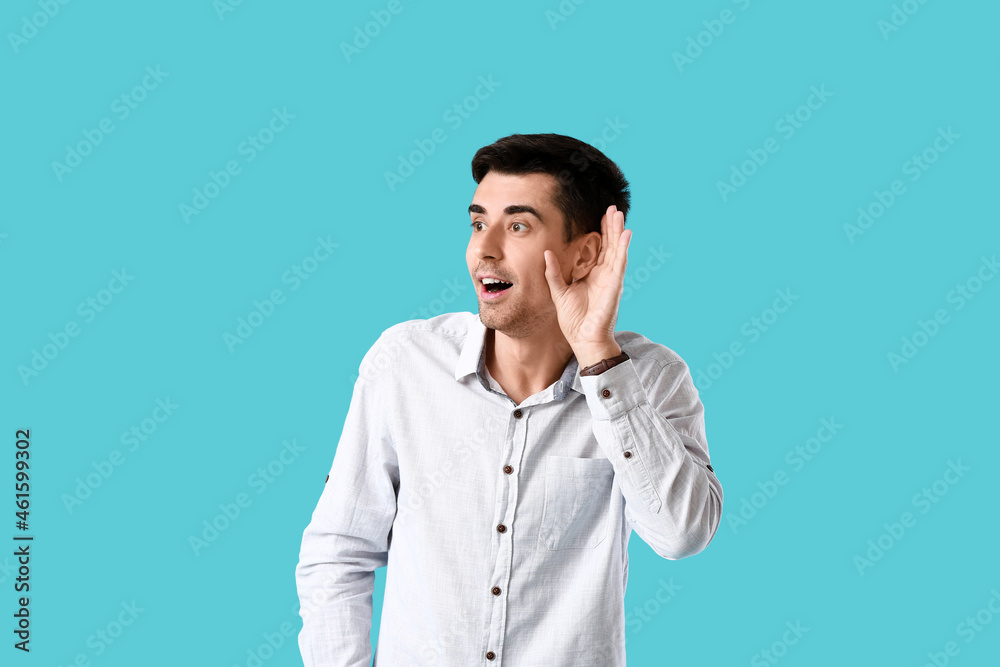 Young gossip man trying to hear something on blue background Young gossip man trying to hear something on blue background