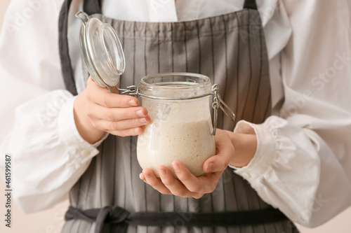 Woman holding glass jar of fresh sourdough on light background, closeup