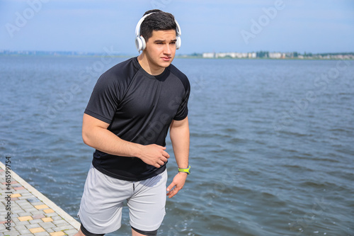 Muscular young man in headphones running near river
