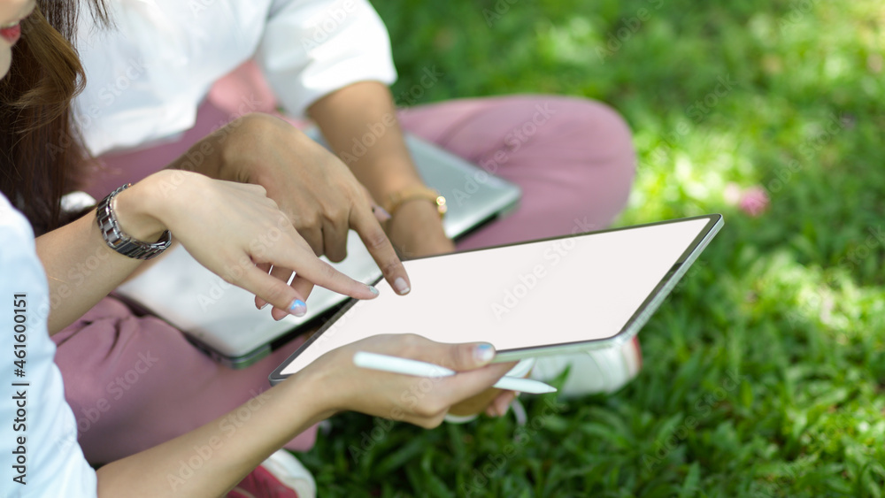 Naklejka premium Cropped image of two of female friends sits in a city park looking on digital tablet