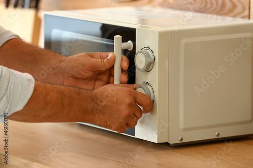 Mature man heating food in microwave oven, closeup
