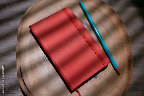 red moleskine with pencil on wooden background for mockup. flat notebook with elastic on shade of blind curtain photo