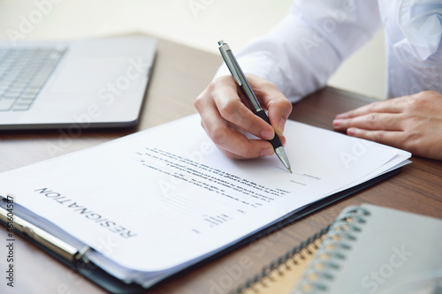 Close up businesswoman hand signing her resignation letter on his desk before sending it to his boss to quit a job. unemployment and change job concept