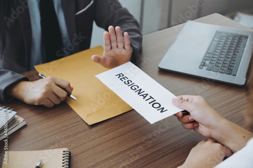 businesswoman hand sending a resignation letter to her boss but the boss raised his hand refusing her from leaving. change of job, unemployment, resign concept. photo