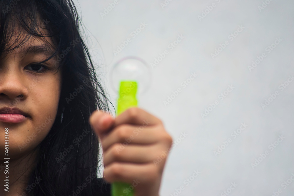 A girl holding a bubble maker and blowing them out.  Image focused on the girl.