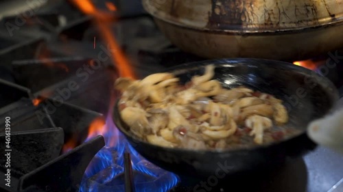 Restaurant stove flares up flames while chef sautes wild mushrooms in pan, cook holds steel pan with towel as and swirls mushooms around fiery skillet, slow motion HD photo