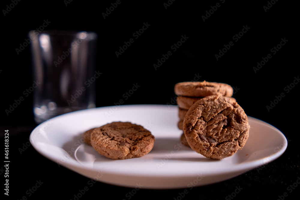 Stacked cookies on white plate and empty glass with black background Stacked cookies on white plate and empty glass with black background