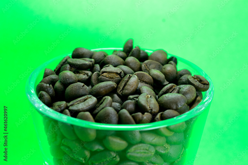 Coffee beans in a transparent glass on a clean green background Coffee beans in a transparent glass on a clean green background