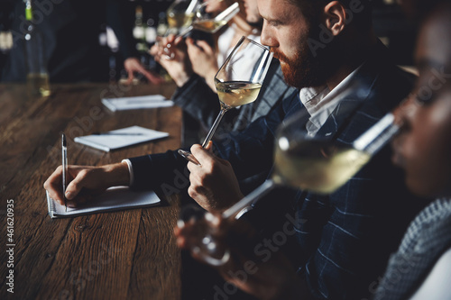 Caucasian man and african woman sommelier bartender smelling white wine and making degustation card photo