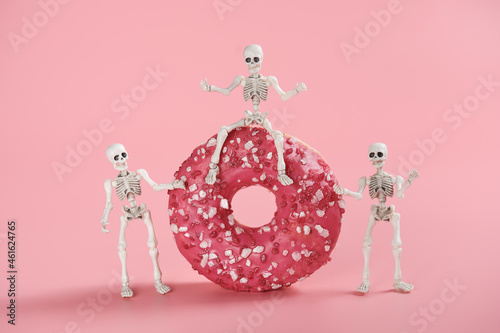 The skeleton sits astride a pink-glazed donut and two skeletons stand side by side. Bright image on a pink background for a Halloween party in a cafe