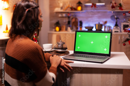 Caucasian adult looking at laptop computer with green screen modern technology for mockup template gadget. Young festive woman using device for digital chroma key isolated display