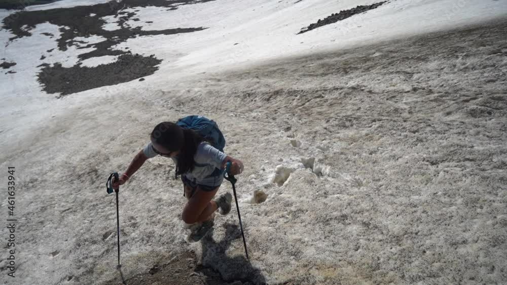 Woman With Trekking Poles Walking Uphill on Snow in Mountain Landscape on Sunny Summer Day, Slow Motion Woman With Trekking Poles Walking Uphill on Snow in Mountain Landscape on Sunny Summer Day, Slow Motion