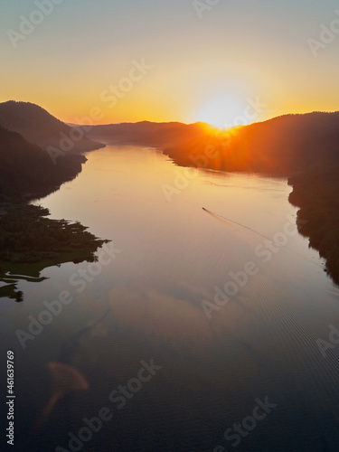 The western shore of Lake Teletsky is set at sunset, the setting sun tingles white cumulus clouds orange. photo