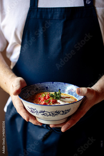 Chef holding a bowl of japanese curry chicken ramen with tomatoes