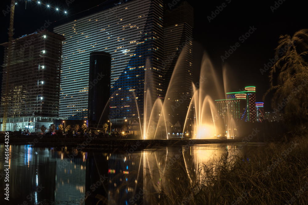 Singing light and music fountain on background of panorama of beautiful buildings at night.