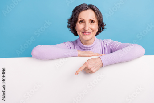 Photo of eldely woman happy positive smile point finger empty space banner ad suggest advice isolated over blue color background photo