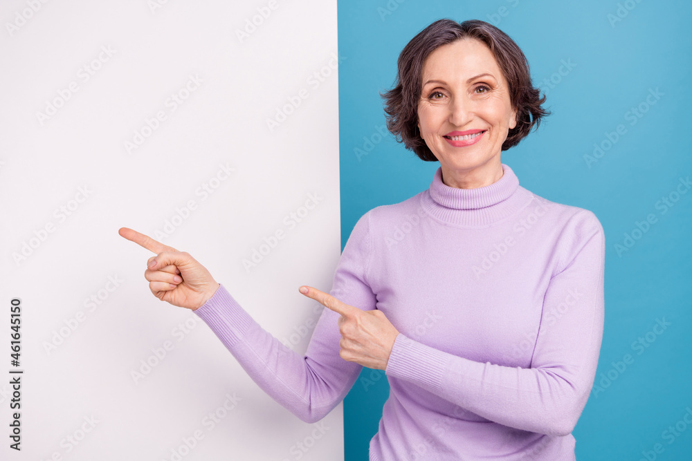 Photo of elderly woman happy positive smile point fingers paper placard advertise recommend isolated over blue color background Photo of elderly woman happy positive smile point fingers paper placard advertise recommend isolated over blue color background