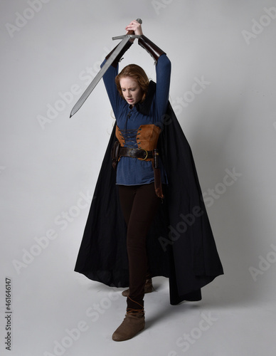 Fotografie Full length, portrait of red haired woman wearing medieval viking inspired costume and flowing cloak,  Holding a long sword weapon  posing against studio background