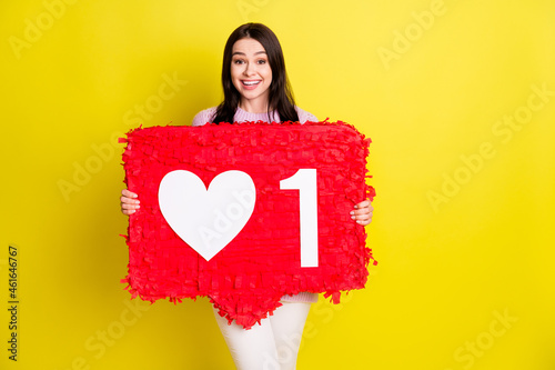 Astonished young lady hold big red toy wear white pants isolated on vivid yellow color background