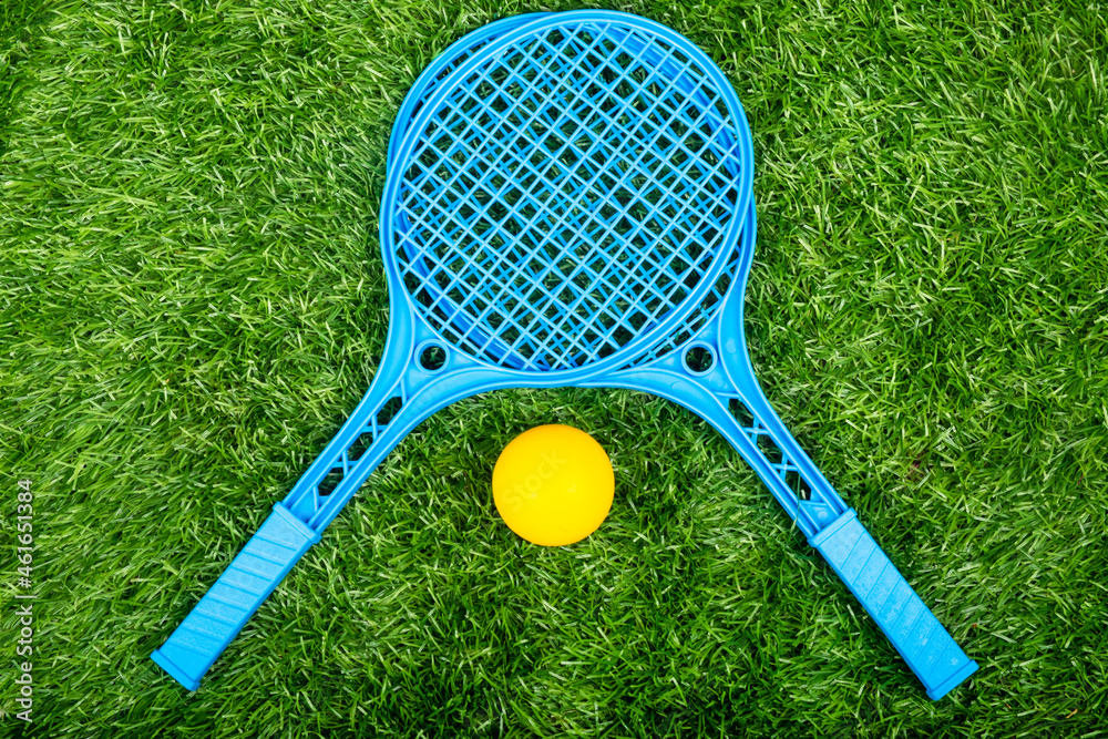 children tennis rackets and a ball on a green lawn, summer outdoor sport activities
