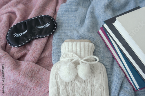 Eine Wärmflasche, eine Schlafmaske und ein Bücherstapel auf einem Bett. Winter, Hygge.
