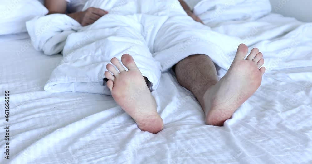 Morning and waking up. Feet under the covers in bed in the morning. Men's feet under the covers in a white bed. Morning and waking up. Feet under the covers in bed in the morning. Men's feet under the covers in a white bed.