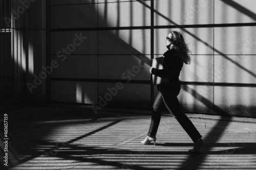 Business woman with a laptop goes straight ahead, sunlight and diagonal shadows. 