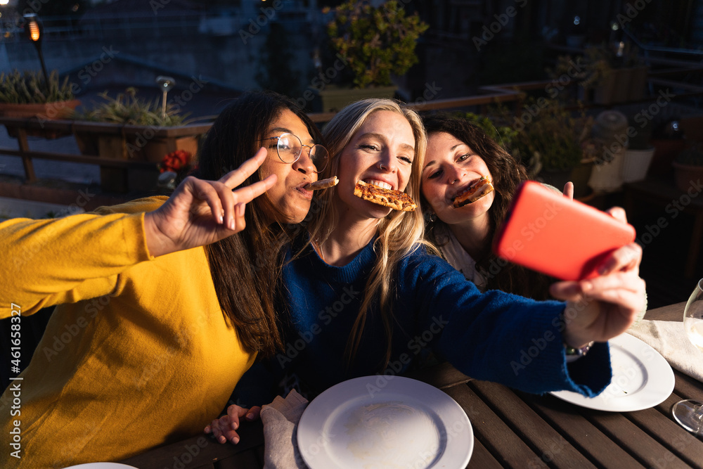 Happy friends eating pizza and taking a selfie with their mobile phone.