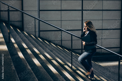 Business woman with a laptop goes up stairs to modern building, woman has phone in the hand. 