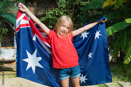 Happy Australia Day concept. Smiling caucasian child girl holding waving national flag. Patriot kids celebrate Australia Day outside.