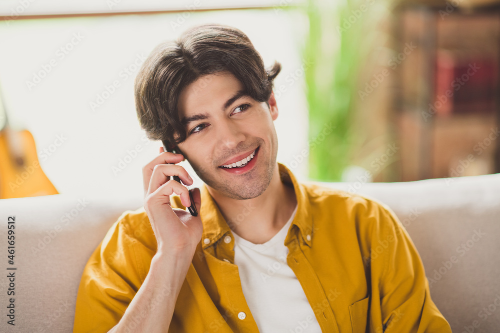 Photo of positive dream glad guy hold telephone make call sit cozy couch wear yellow shirt home indoors Photo of positive dream glad guy hold telephone make call sit cozy couch wear yellow shirt home indoors