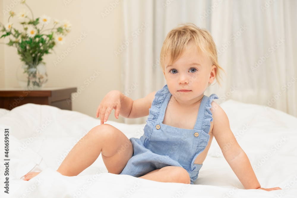 Pretty caucasian blonde baby girl of 1-2 years old sit on white blanket,look at camera posing like model.Beautiful infant wear stylish blue body.Concept of sheets or child before going to bed,wake-up Pretty caucasian blonde baby girl of 1-2 years old sit on white blanket,look at camera posing like model.Beautiful infant wear stylish blue body.Concept of sheets or child before going to bed,wake-up