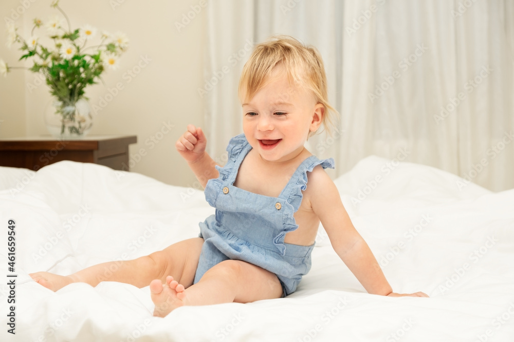 Pretty smiling caucasian blonde baby girl of 1-2 years old sit on white blanket,laugh in bedroom.Cute kid having fun,emotional child,Concept of good sheets or infant before going to bed or wake-up Pretty smiling caucasian blonde baby girl of 1-2 years old sit on white blanket,laugh in bedroom.Cute kid having fun,emotional child,Concept of good sheets or infant before going to bed or wake-up
