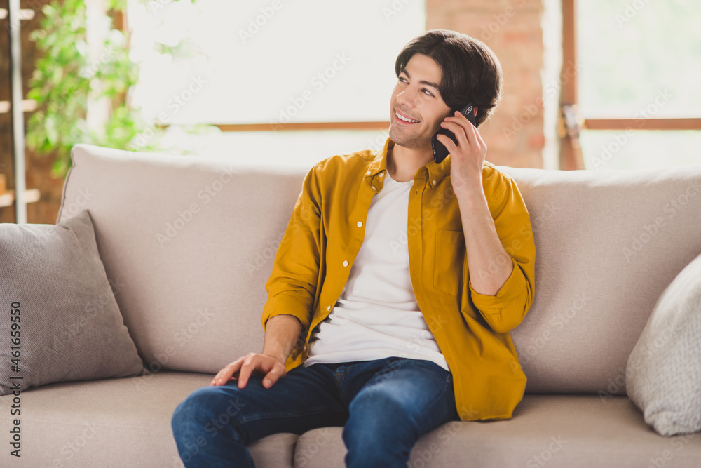 Photo of cheerful inspired positive guy hold telephone have conversation sit couch wear yellow shirt home indoors