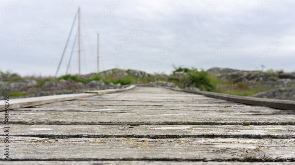 Fototapeta premium Empty wooden bridge leading toward small island with visible mast of sailboat in the background