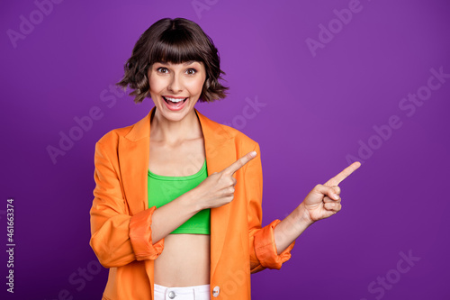 Photo of impressed funny young woman dressed orange blazer pointing fingers empty space smiling isolated purple color background