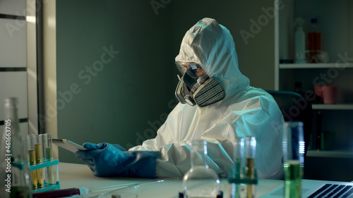 Male cientist in protective uniform and respirator using digital tablet in lab photo