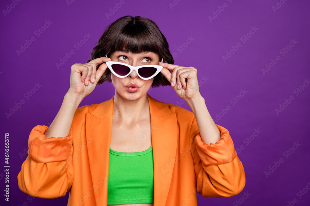 Photo of excited funny young woman dressed orange blazer arms dark eyewear looking empty space isolated purple color background Photo of excited funny young woman dressed orange blazer arms dark eyewear looking empty space isolated purple color background