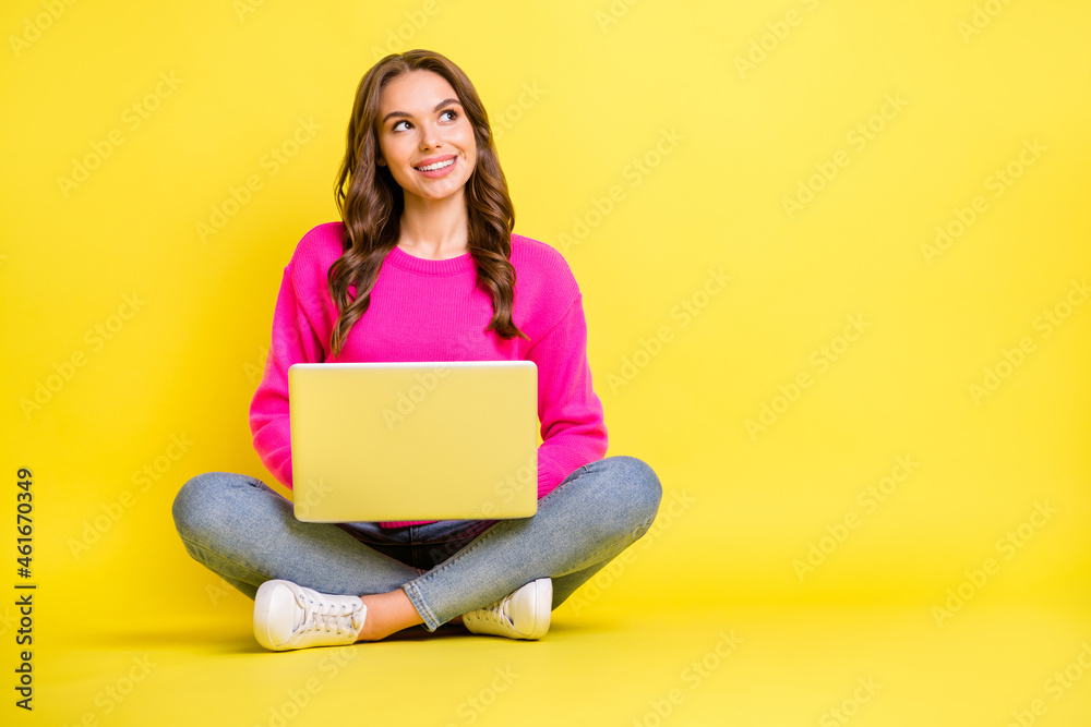 Full size photo of young happy positive dreamy smiling girl look copyspace sit floor work laptop isolated on yellow color background Full size photo of young happy positive dreamy smiling girl look copyspace sit floor work laptop isolated on yellow color background