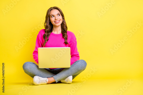 Full size photo of young happy positive dreamy smiling girl look copyspace sit floor work laptop isolated on yellow color background © deagreez