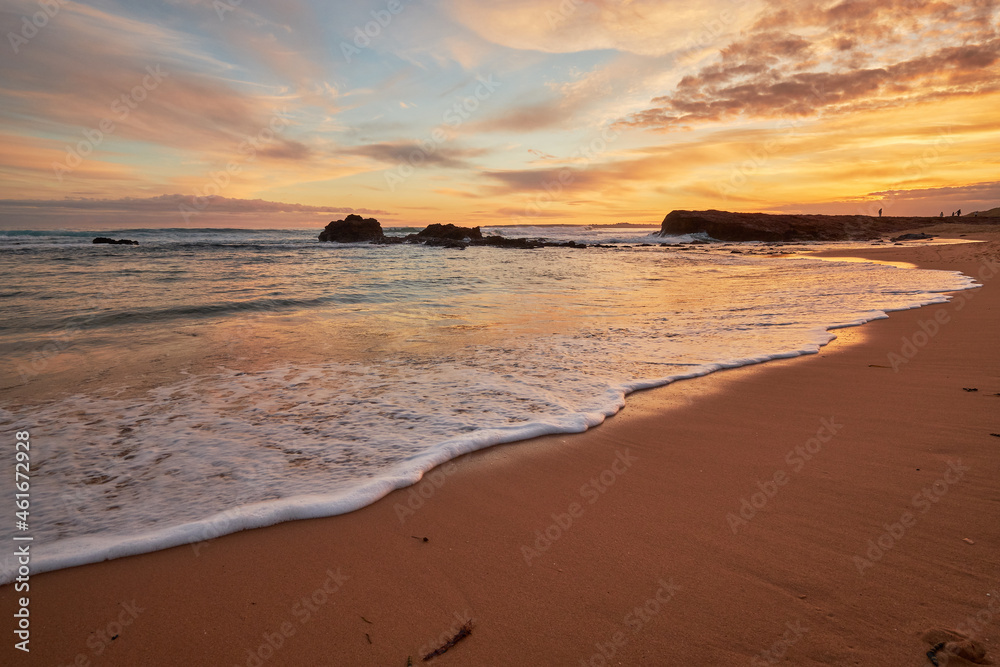 A beautiful beach sunset illuminating the sky with vibrant orange colours, a scenic view of the ocean with waves washing onto the shore along the coast of Phillip Island, Australia.
