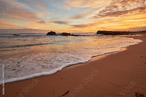 A beautiful beach sunset illuminating the sky with vibrant orange colours, a scenic view of the ocean with waves washing onto the shore along the coast of Phillip Island, Australia. 