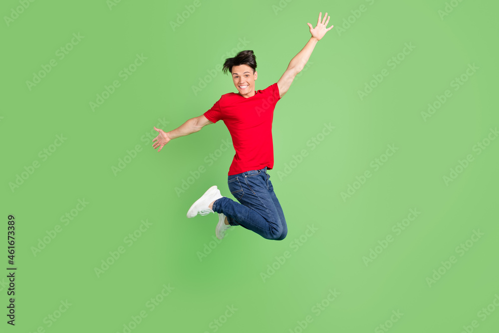 Photo of funky charming young man wear red t-shirt smiling jumping high isolated green color background