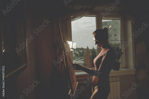 A beautiful girl is dressed in a bodysuit. The girl the artist draws on the easel.