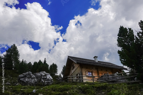 wooden alpine hut with a fence on a hill with amazing clouds on the sky © thomaseder